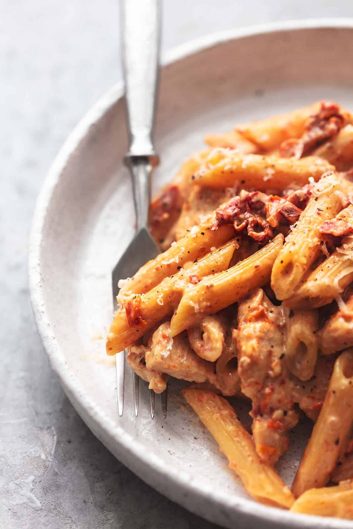 close up of creamy sun-dried tomato chicken pasta with a fork underneath on a plate.