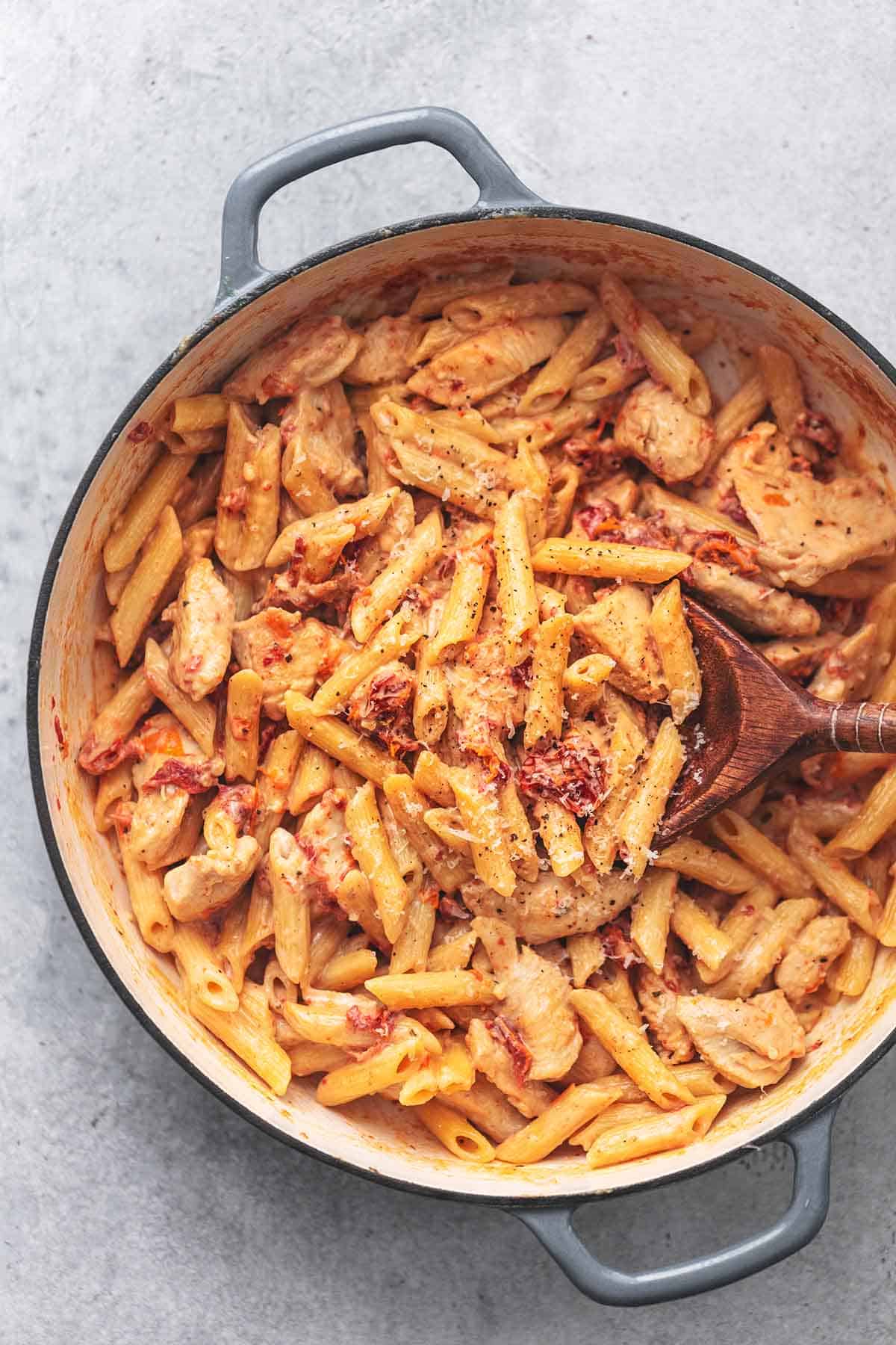 top view of creamy sun-dried tomato chicken pasta with a serving spoon in a skillet.