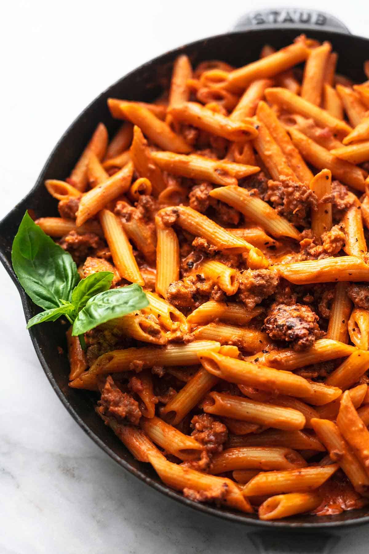 close up top view of creamy tomato sausage penne with fresh basil in a skillet.