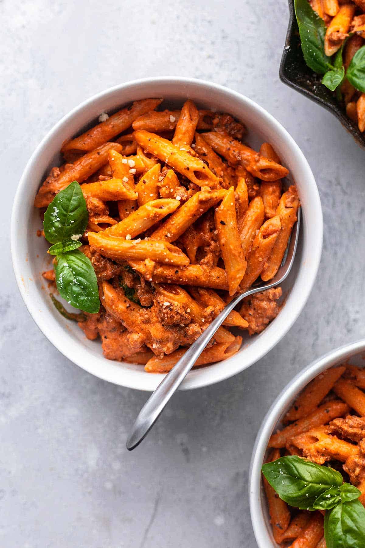 bowl of creamy tomato sausage penne with fresh basil and a fork.