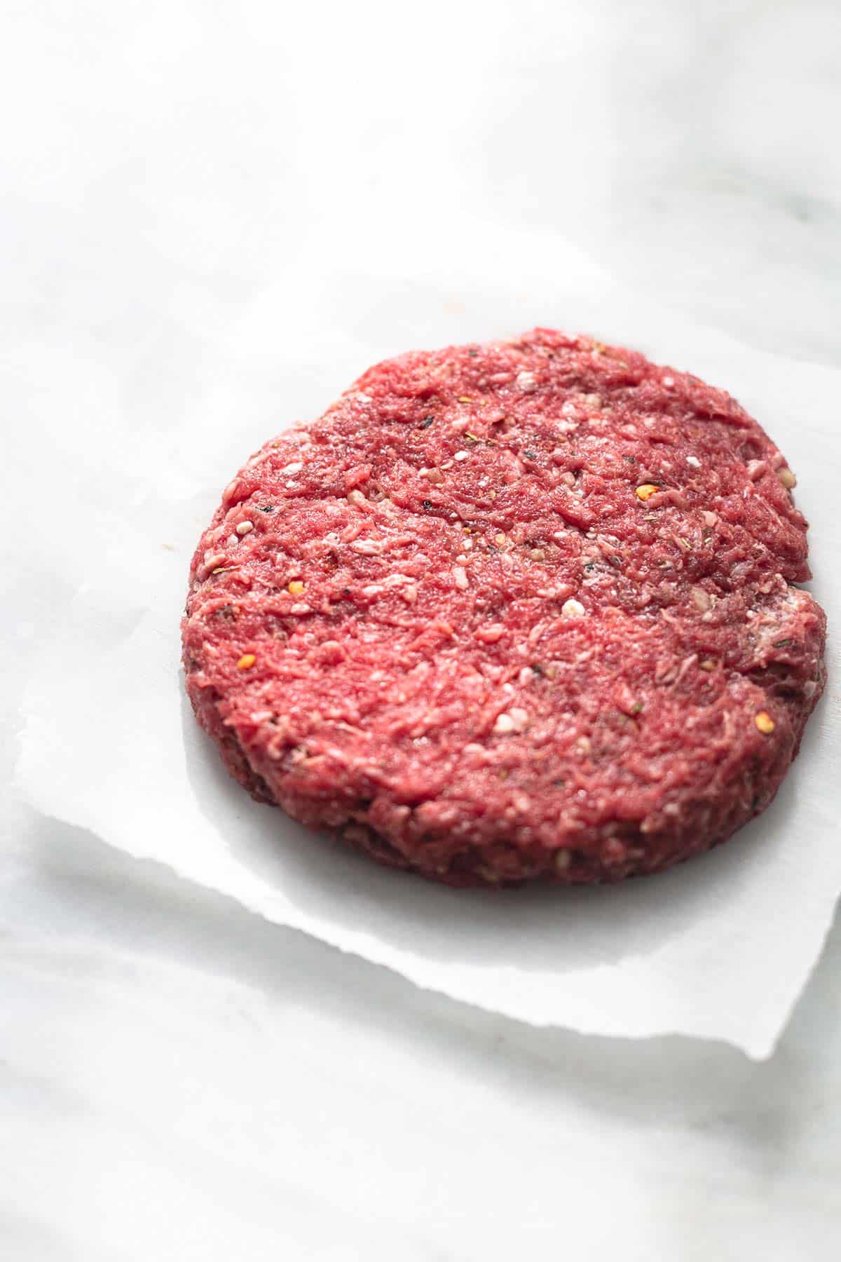 a single ground beef patty on parchment paper.