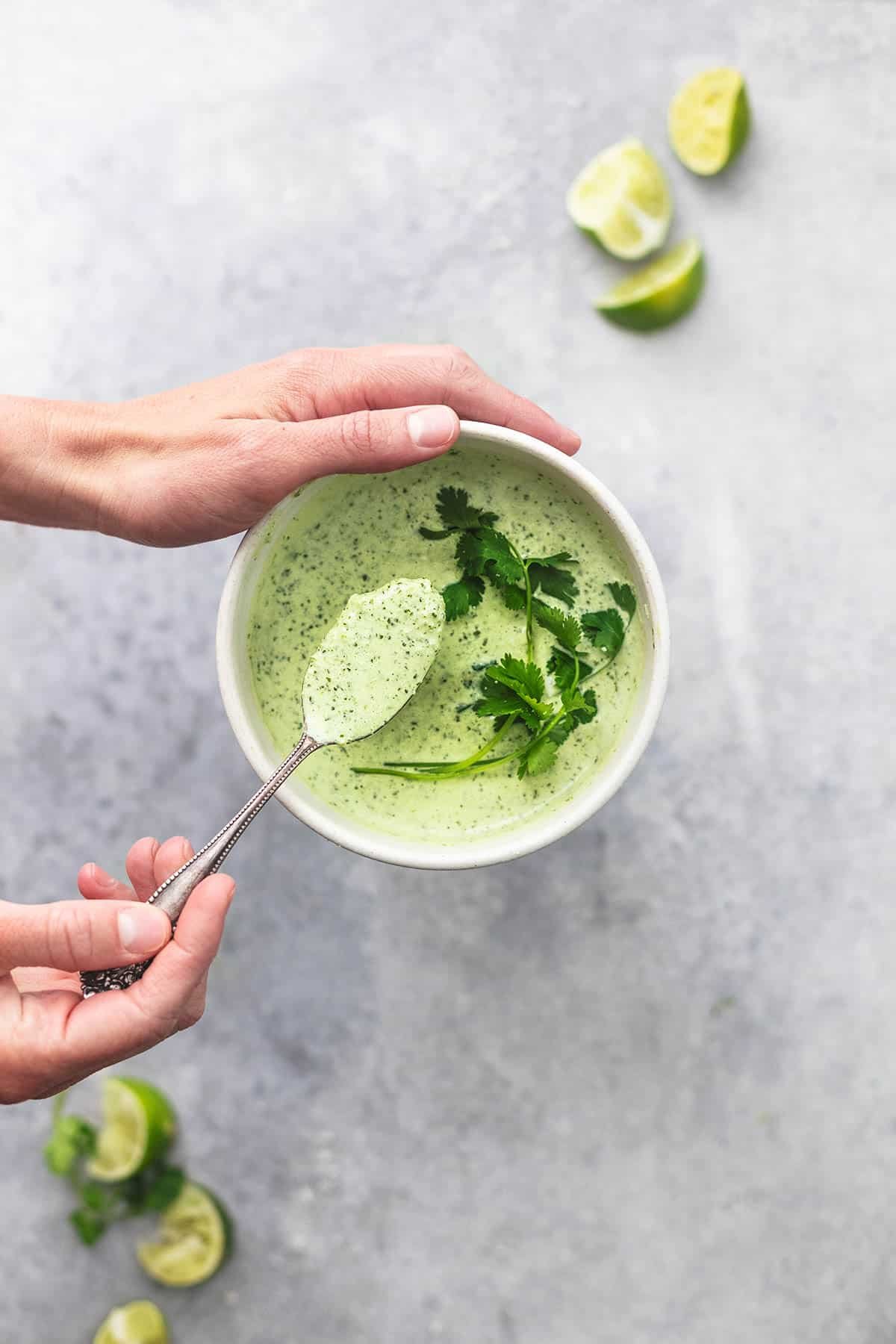 top view of a hand holding the side of a bowl and another holding up a spoon from the bowl with cilantro lime sauce.