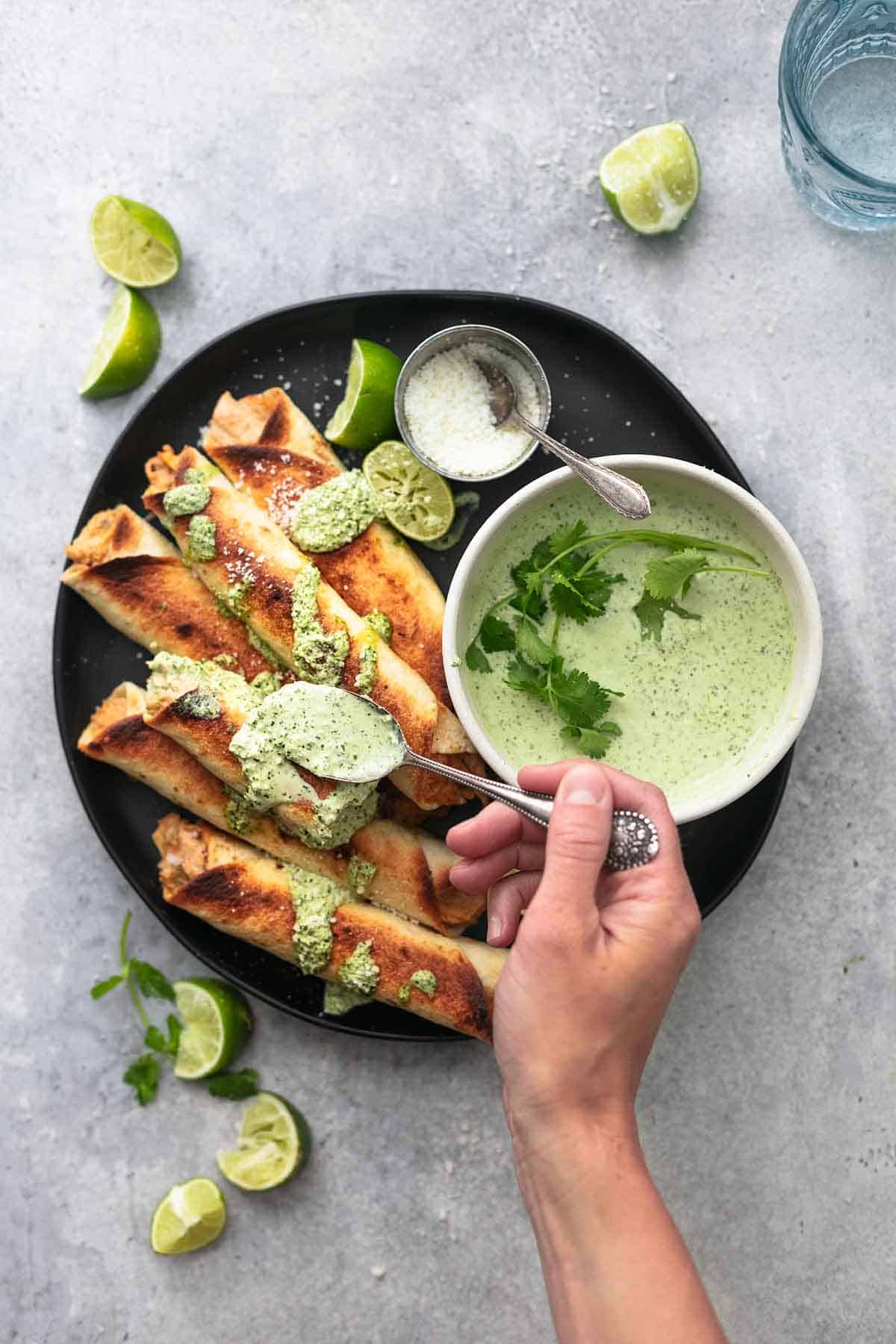 top view of a hand drizzling sauce on instant pot chicken taquitos on a plate.