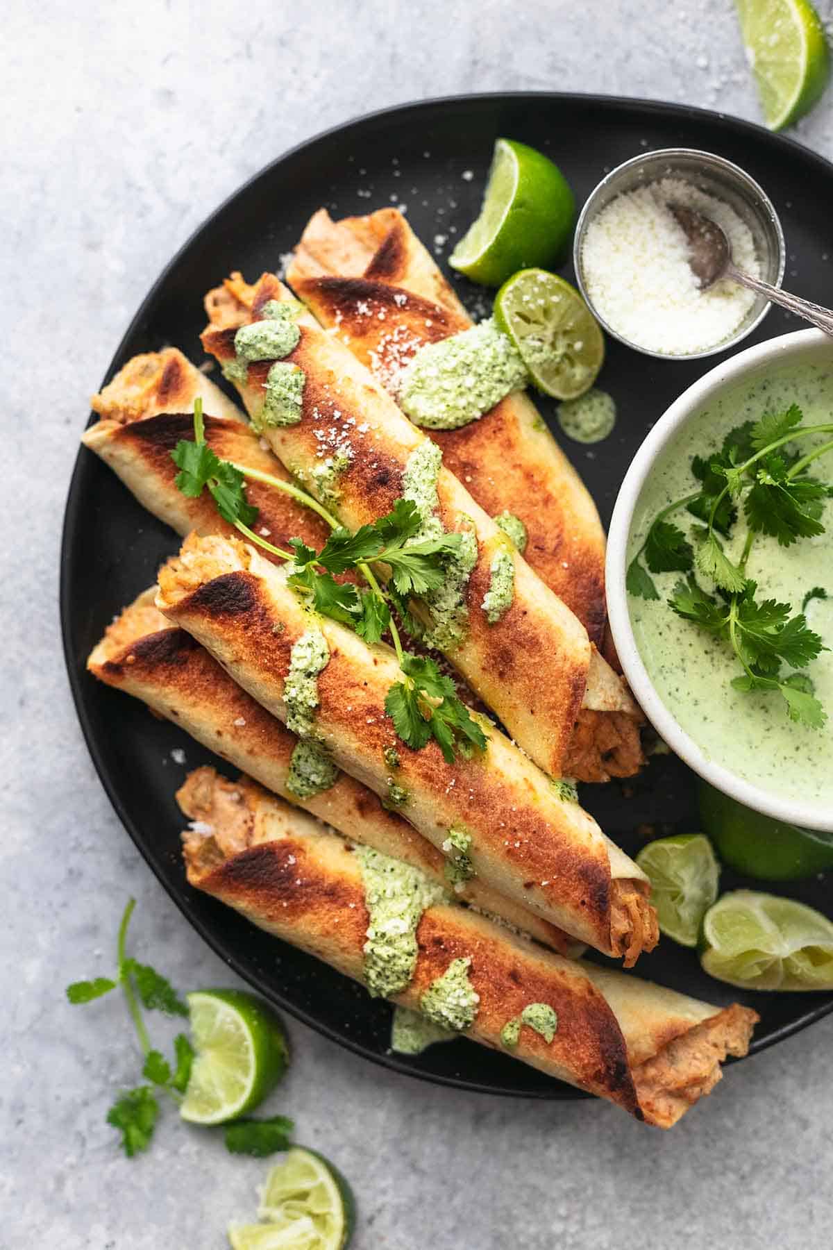 top view of instant pot chicken taquitos on a black plate with lime slices and green sauce.