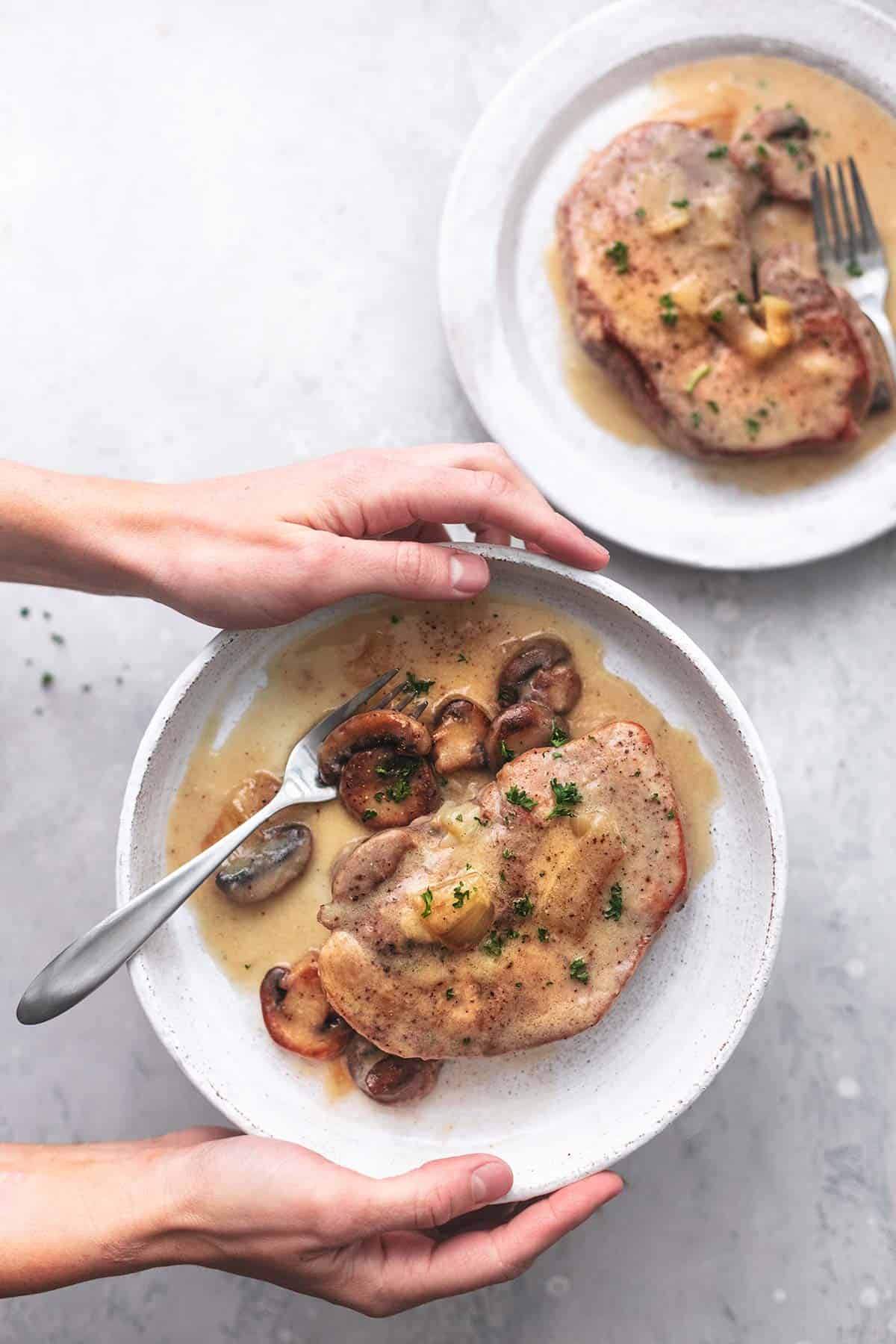 top view of hands holding a plate with instant pot pork chops with gravy and a fork on it with another plate on the side.