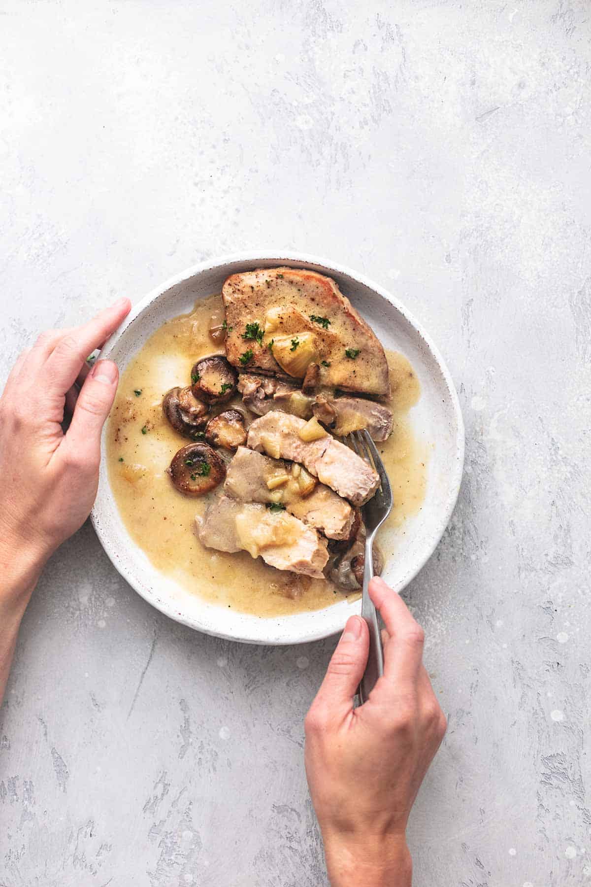 top view of a hand holding the side of a plate with a sliced up instant pot pork chop and gravy on it with another hand holding a fork.