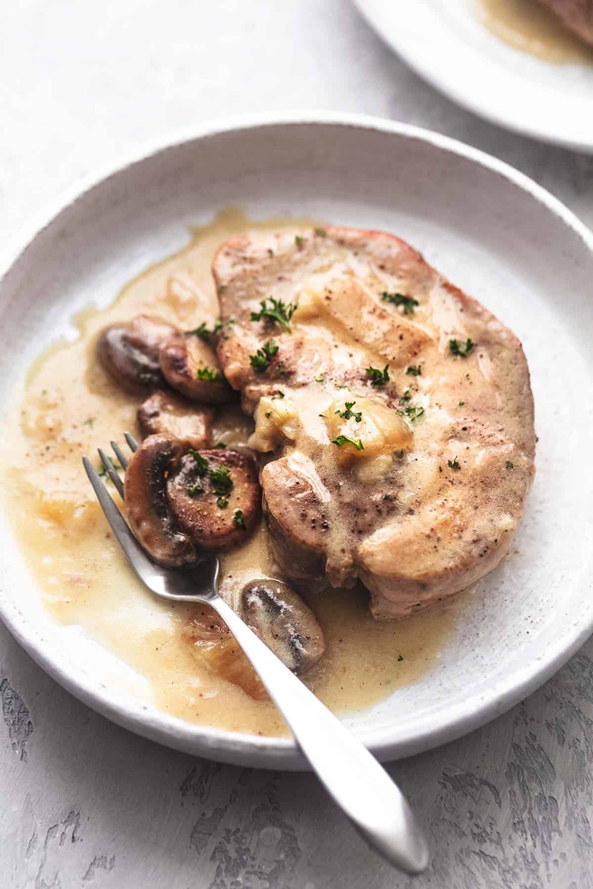 an instant pot pork chop with gravy with a fork on a white plate.