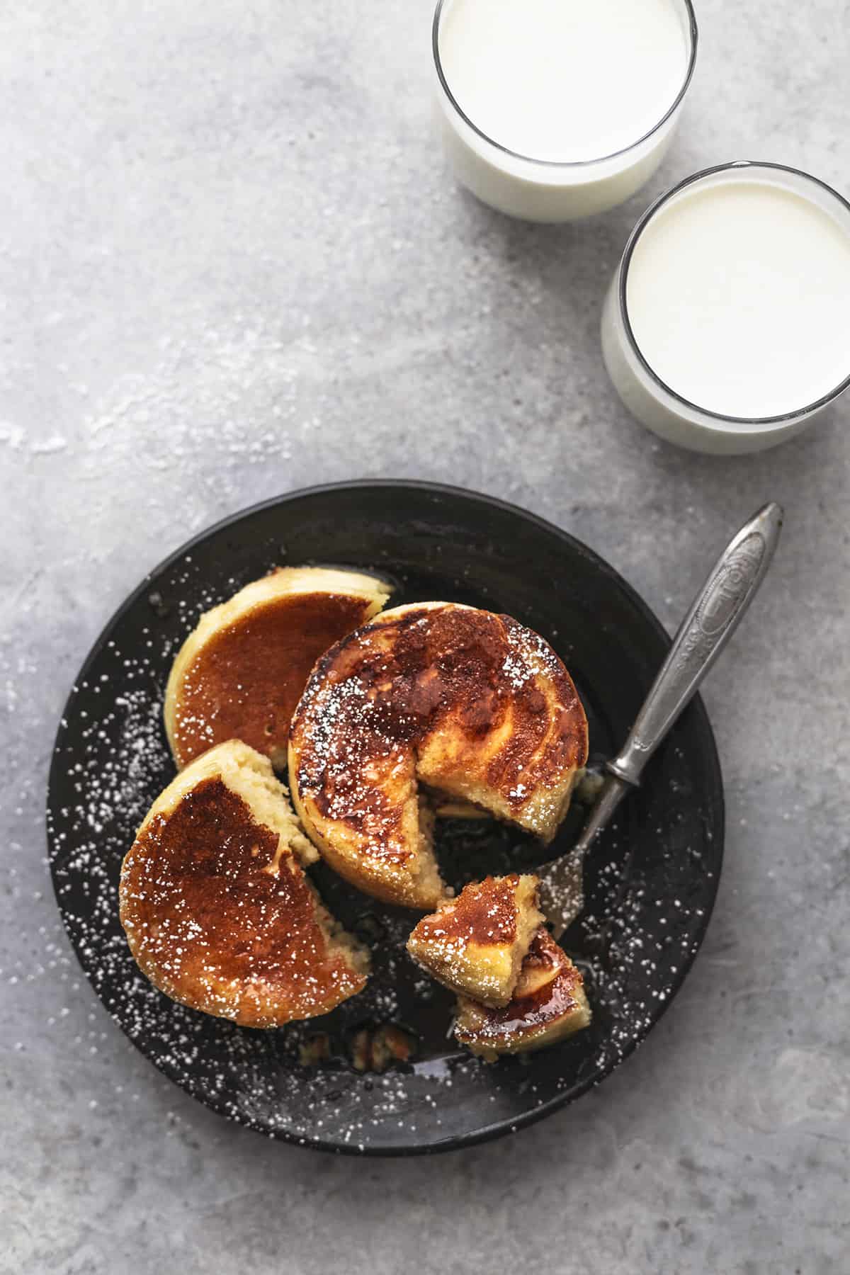 top view of a stack of Japanese soufflé pancakes on a plate with a fork with two glass of milk on the side.