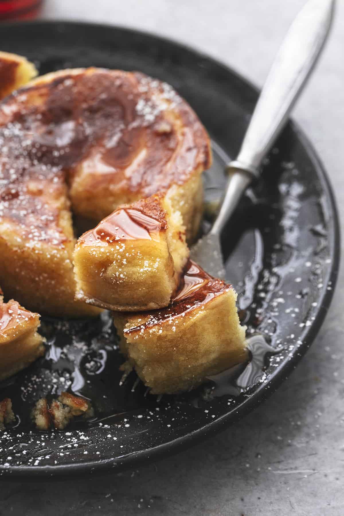 close up of a bite of Japanese soufflé pancakes on a fork on a black plate.