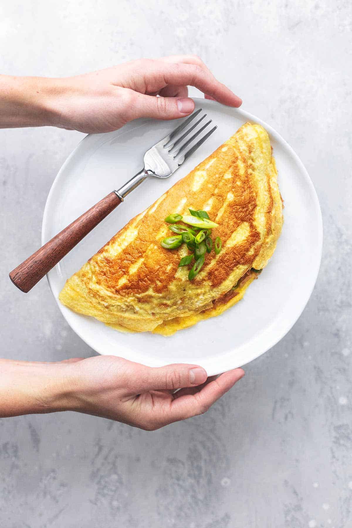 top view of hands holding a plate with a Japanese rice omelet with a fork.