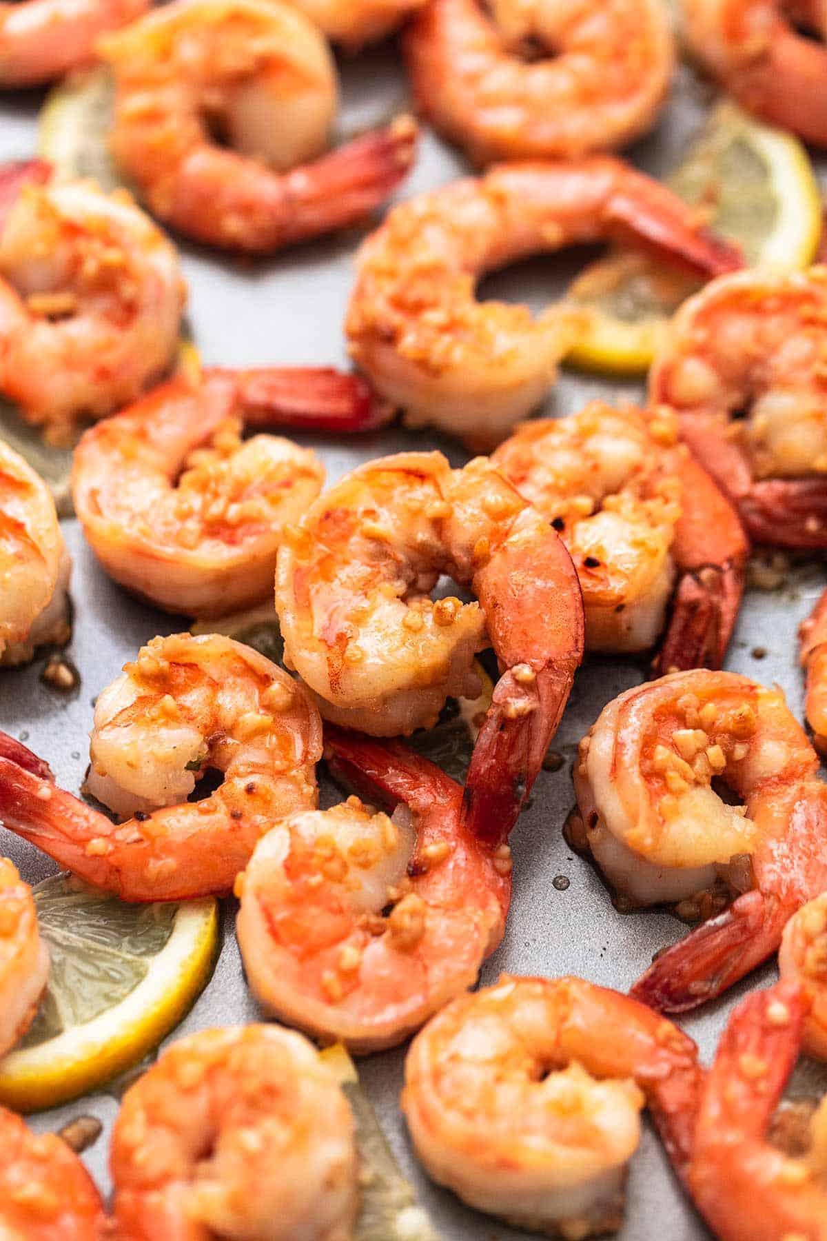 close up of cooked shrimp with lemon and garlic on a sheet pan.