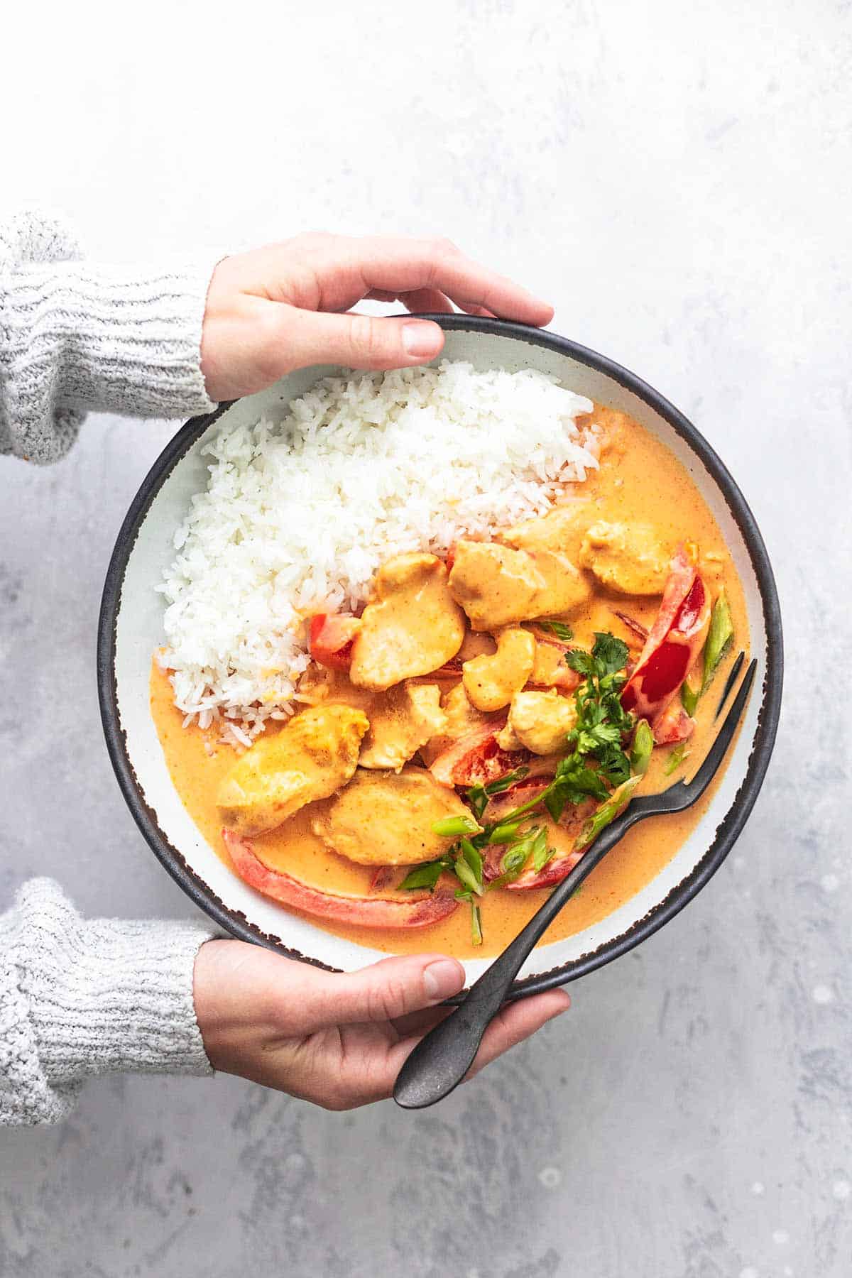 top view of hands holding a plate of Thai chicken curry with coconut milk and rice with a fork.