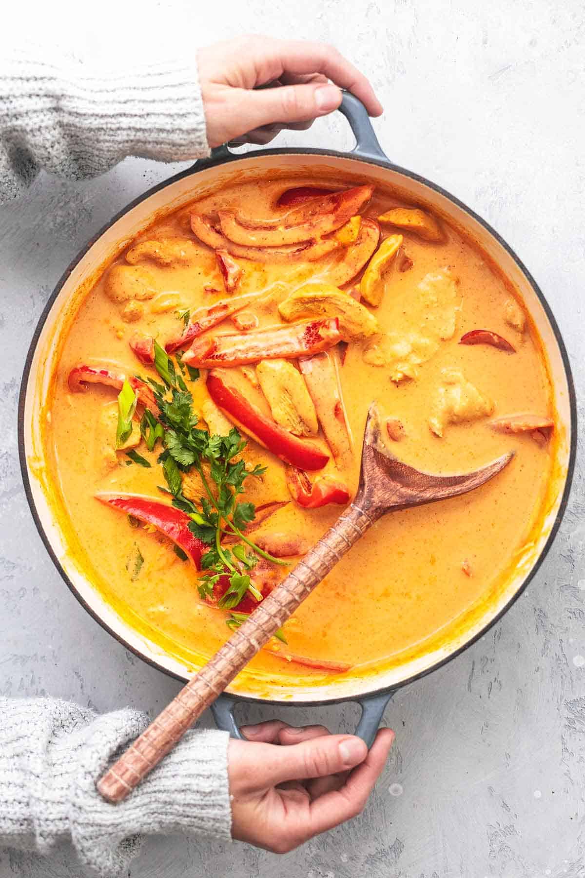 top view of hands holding a skillet with Thai chicken curry with coconut milk with a serving spoon.