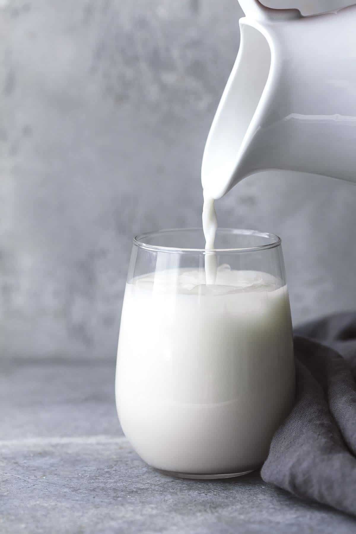 a white pitcher pouring milk into a glass.