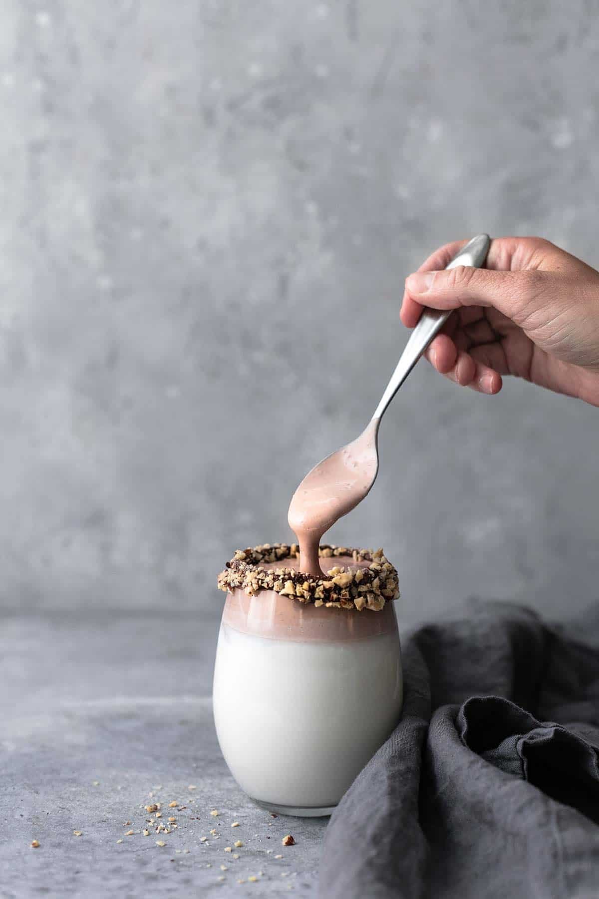 a hand picking up a spoon from a glass of whipped milk: three ways.