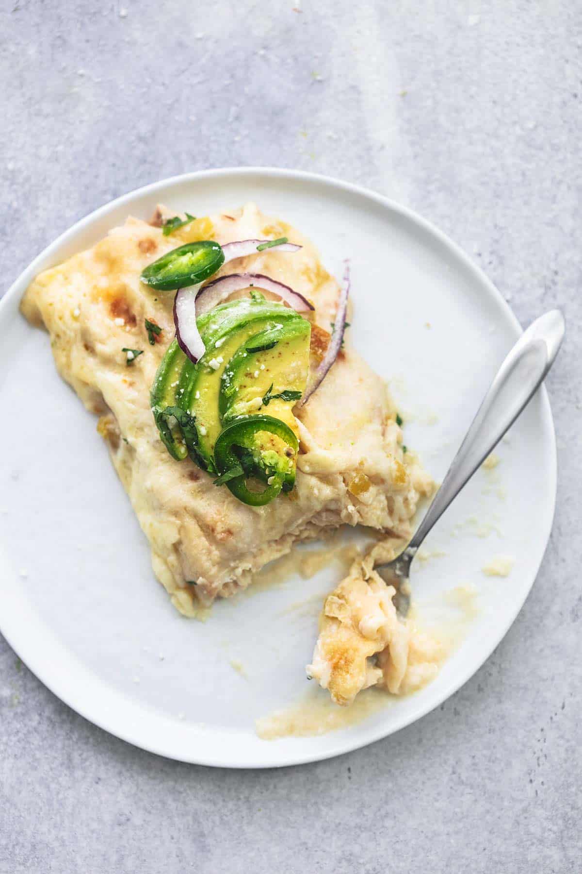 top view of a bite of a creamy white chicken enchilada with the rest of the enchilada on a plate.