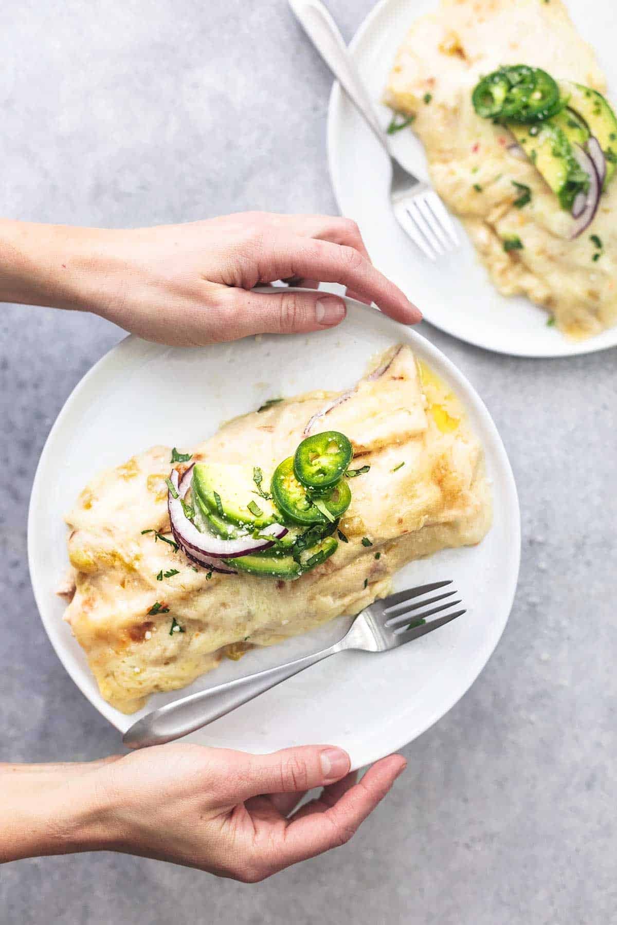 top view of hands holding a creamy white chicken enchilada with a fork on a plate with another plate on the side.