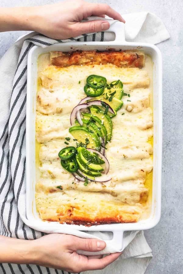 overhead hands holding pan of white chicken enchiladas
