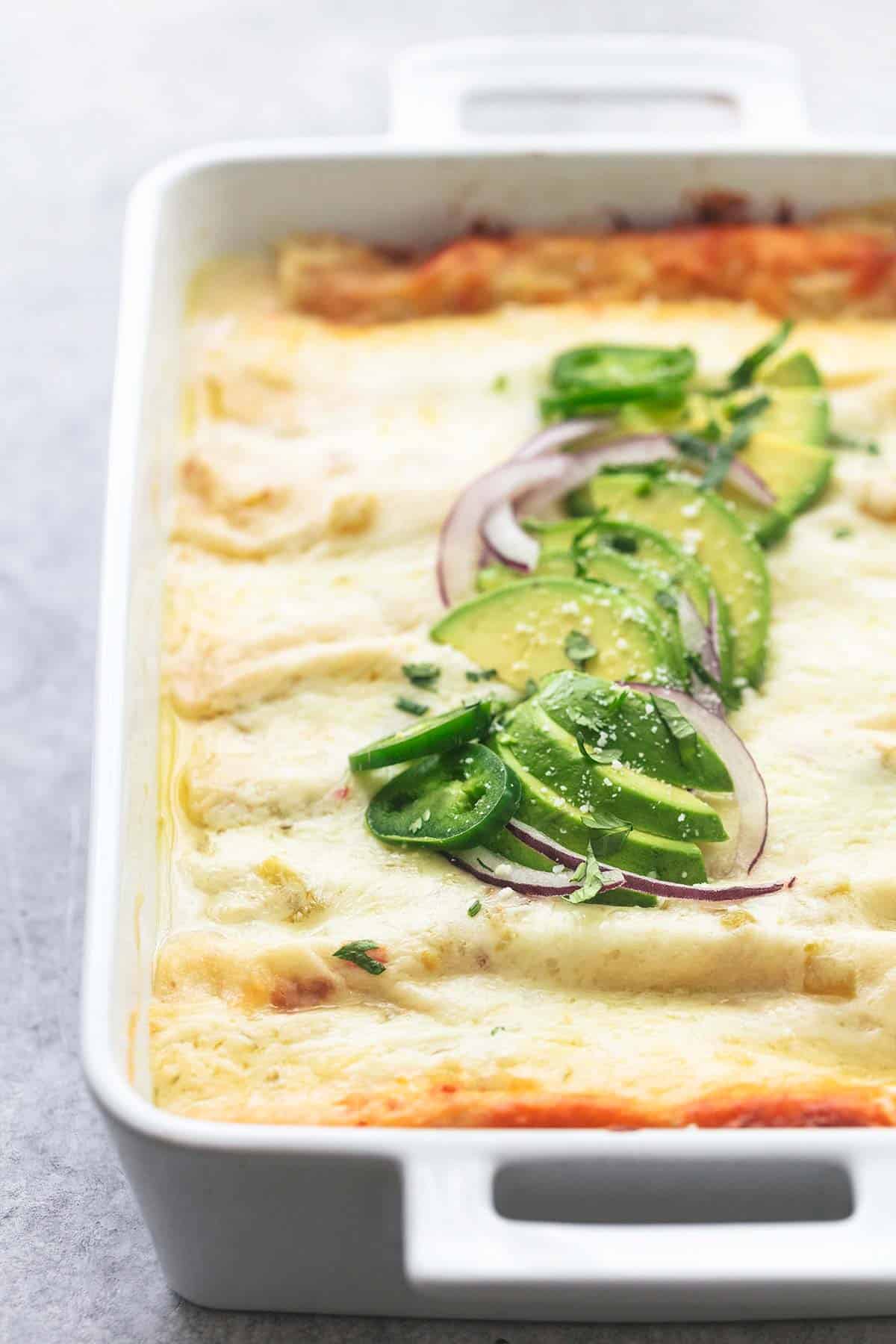 close up of creamy white chicken enchiladas in a pan.