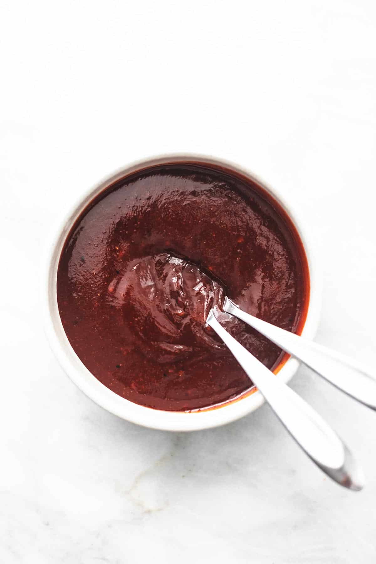 overhead view of bbq sauce in a bowl with two spoons