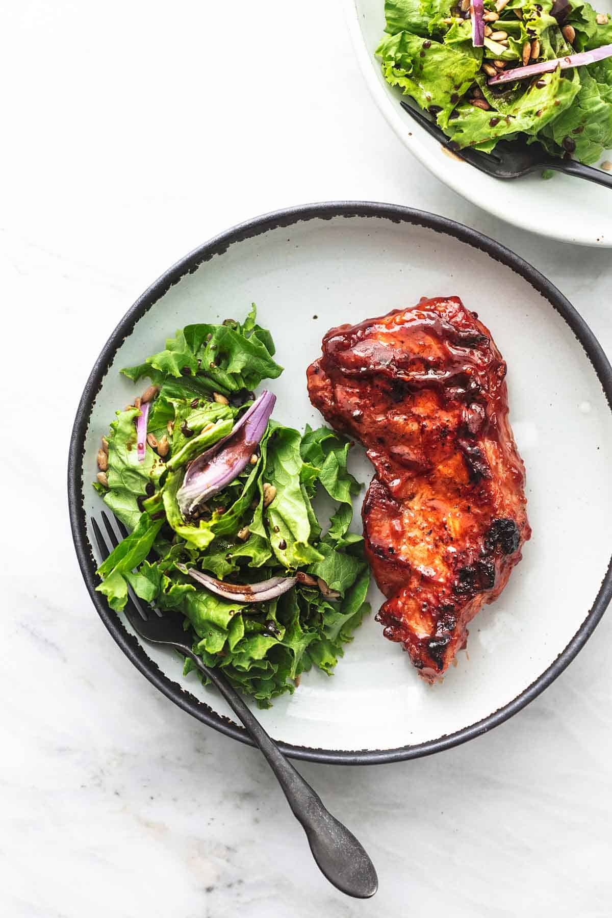 top view of a grilled bbq pork chop with salad and a fork on a plate.