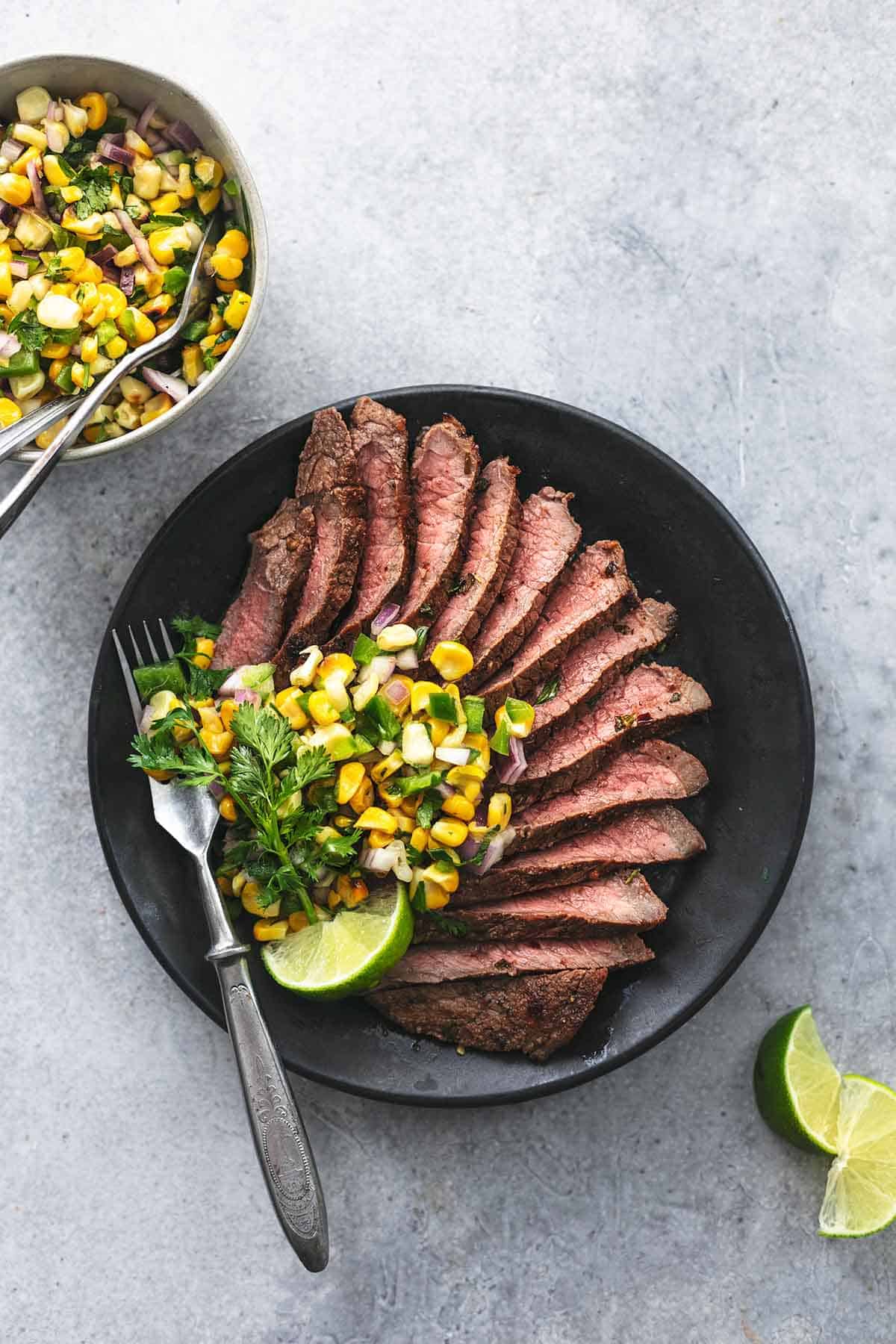 top view of sliced cilantro lime marinated steak with corn salsa and a fork on a plate with more salsa in a bowl on the side.