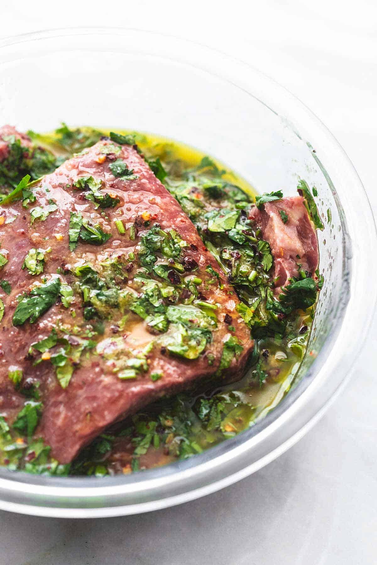close up of steak in cilantro lime marinade in a glass bowl.