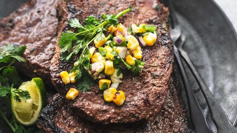 up close view of grilled steak with corn salsa on a black plate with forks