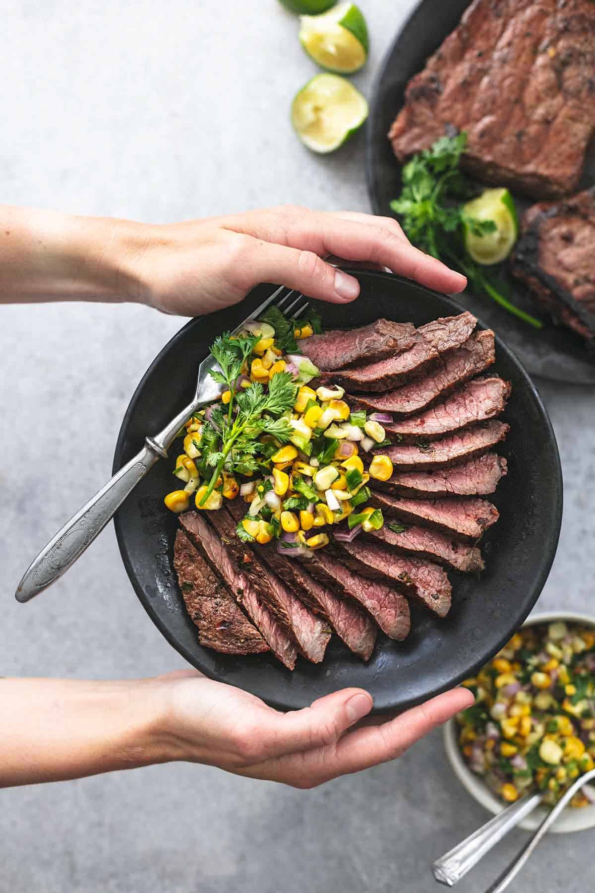 top view of hands holding a plate with cilantro lime marinated steak sliced with corn salsa and a fork.
