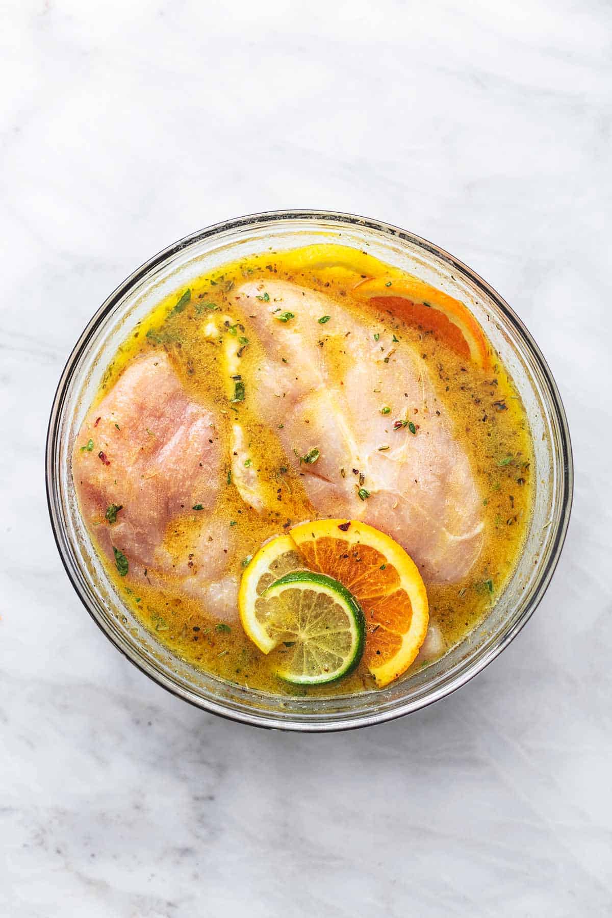 overhead view of raw chicken and lemon slices marinating in bowl