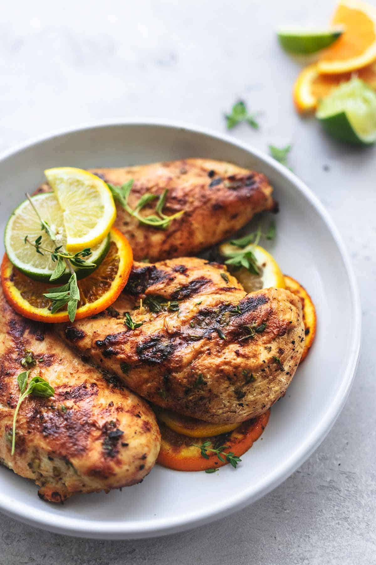 grilled chicken on a white plate with lemon, lime, and orange slices