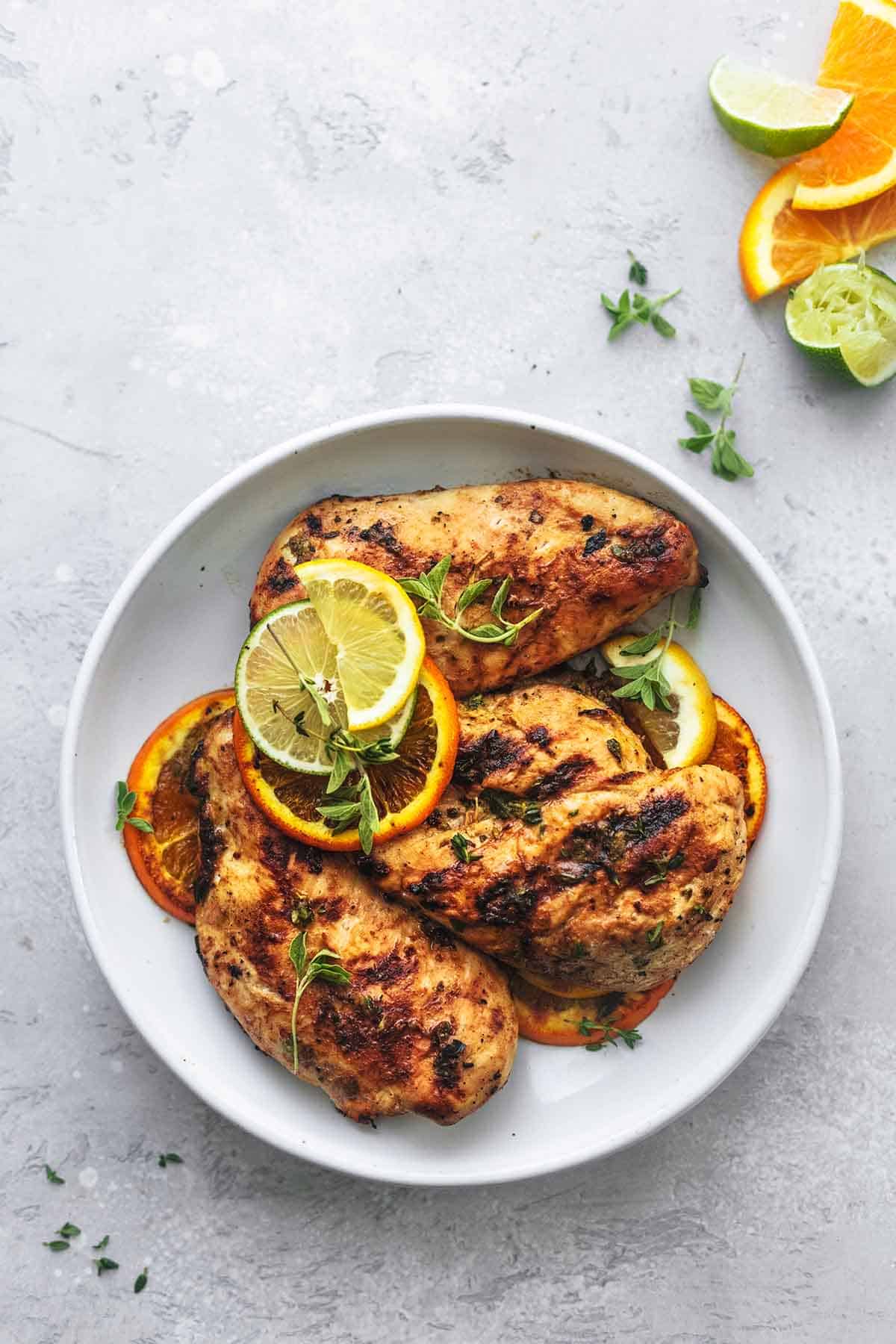 overhead view of grilled chicken on a white plate with lemon, lime, and orange slices