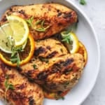 overhead view of grilled chicken on a white plate with lemon, lime, and orange slices
