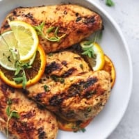 overhead view of grilled chicken on a white plate with lemon, lime, and orange slices