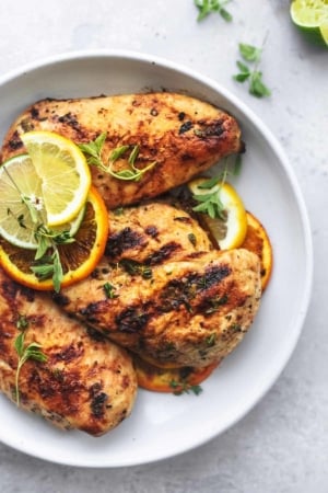 overhead view of grilled chicken on a white plate with lemon, lime, and orange slices