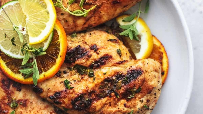overhead view of grilled chicken on a white plate with lemon, lime, and orange slices