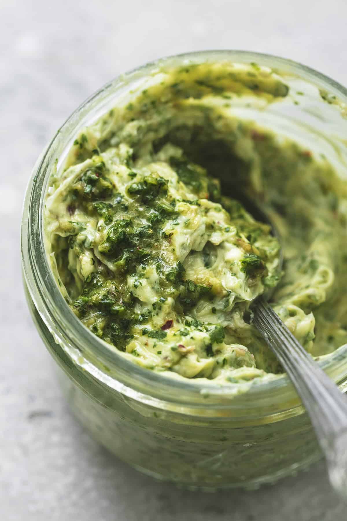 close up of chimichurri butter with a spoon in a jar.