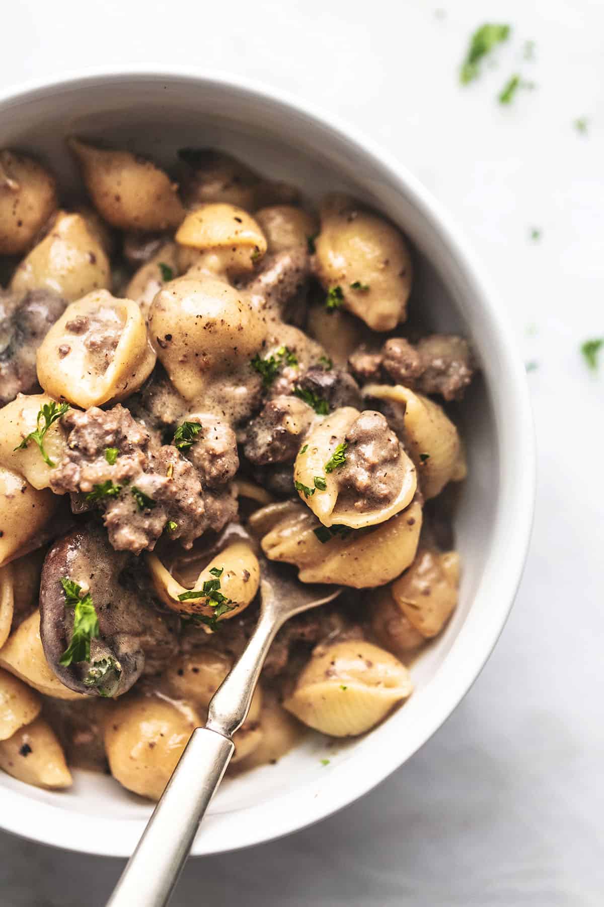 overhead view of half of a white bowl with fork and ground beef stroganoff 