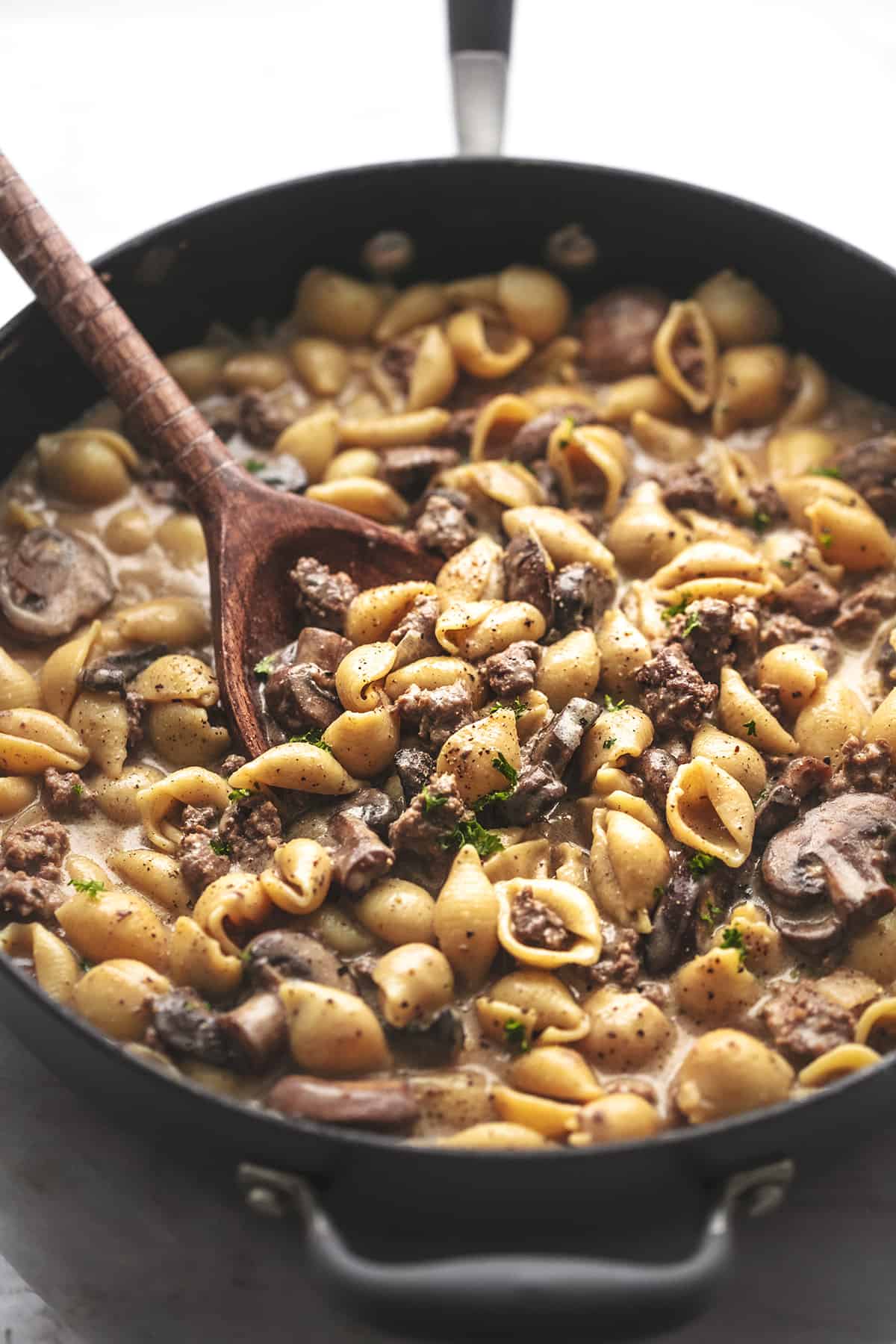 45 degree angle view of skillet filled with pasta shells with ground meat with wooden spoon