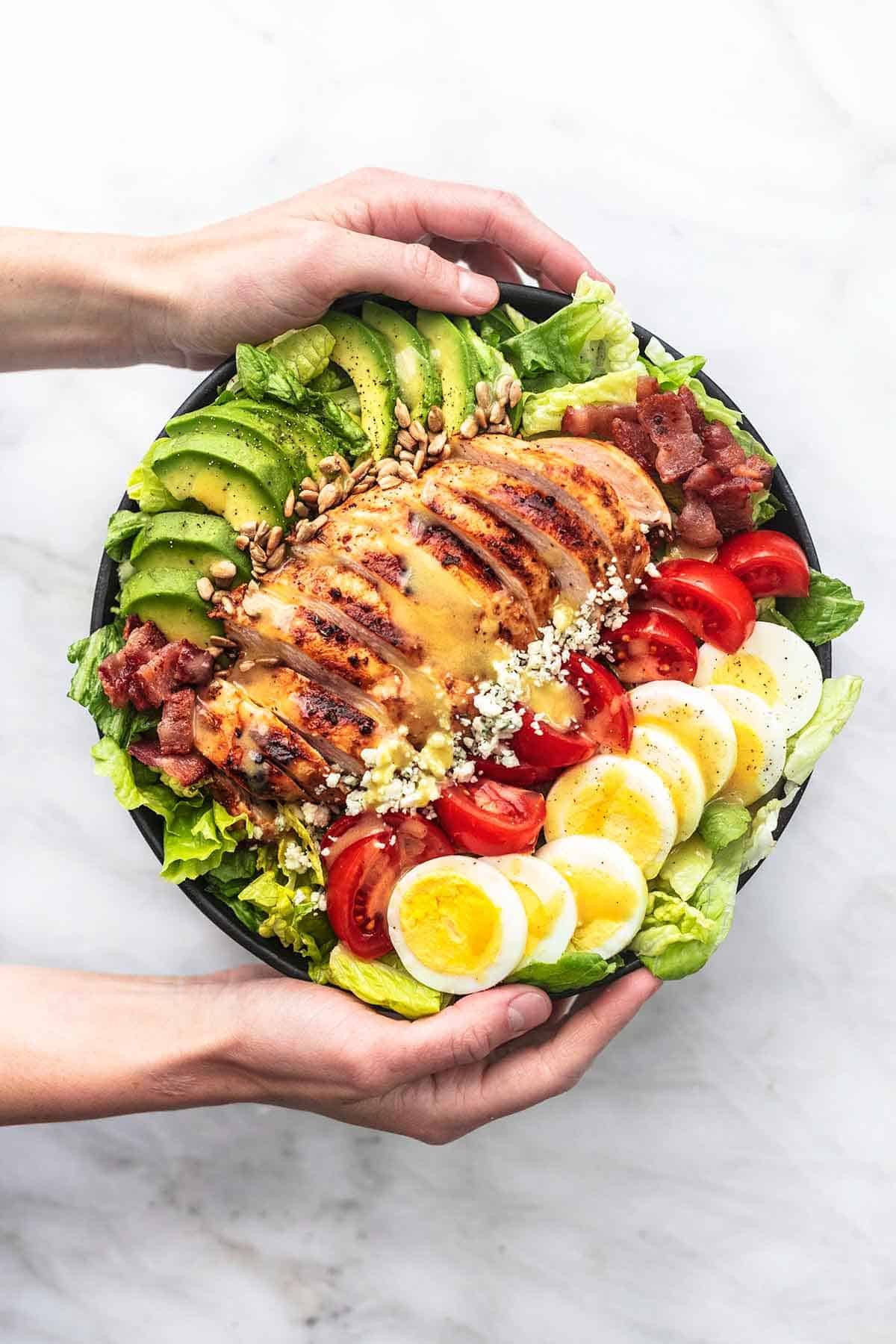 top view of hands holding a bowl of chicken cobb salad.