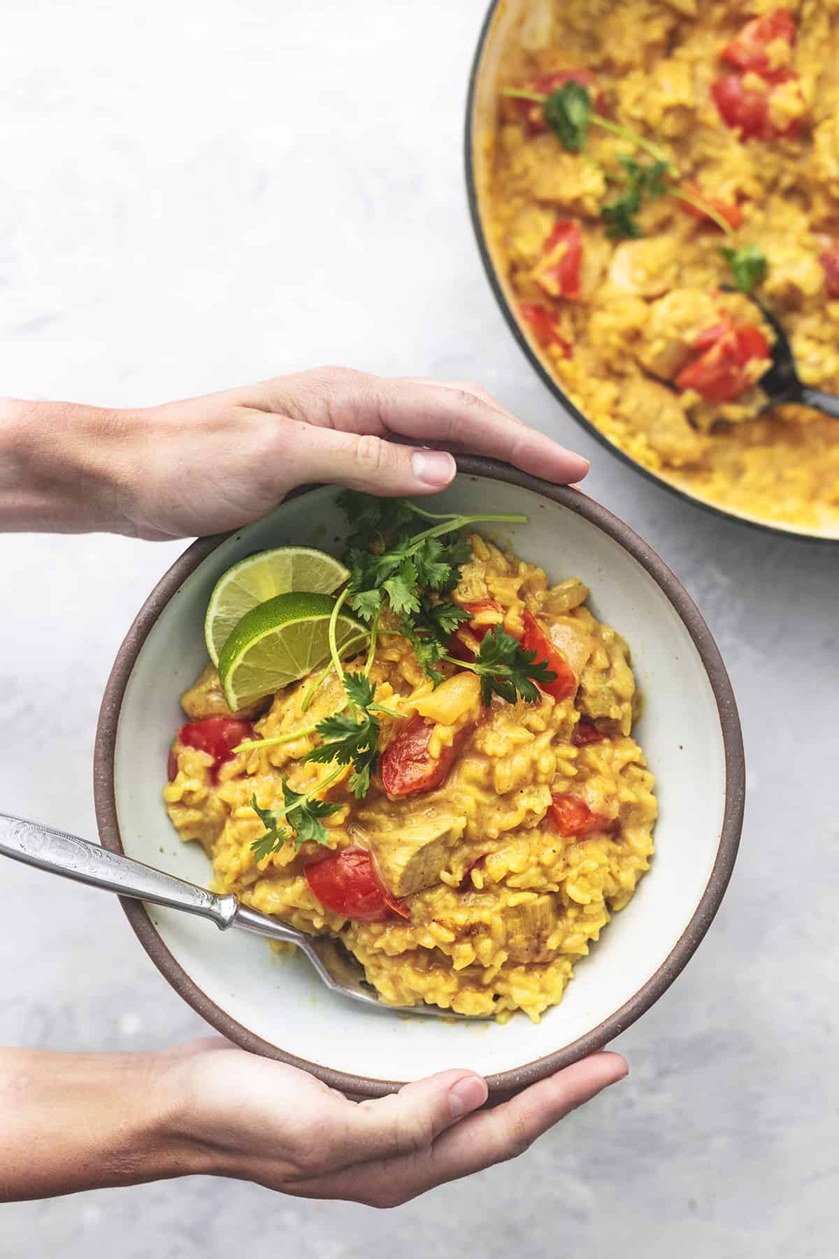 top view of hands holding a bowl of curry chicken and rice with a fork.