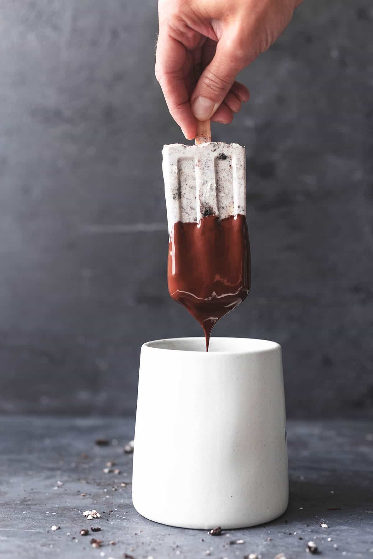 hand dipping popsicle in mug of melted chocolate