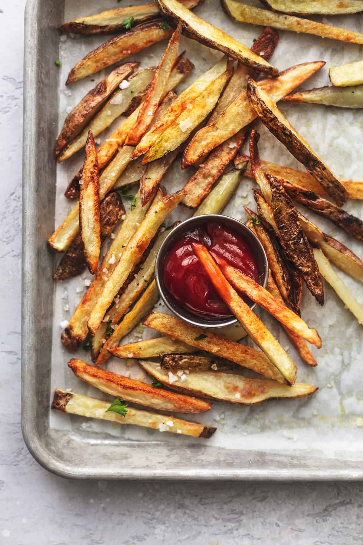 top view of baked french fries on a baking sheet with ketchup in a cup.