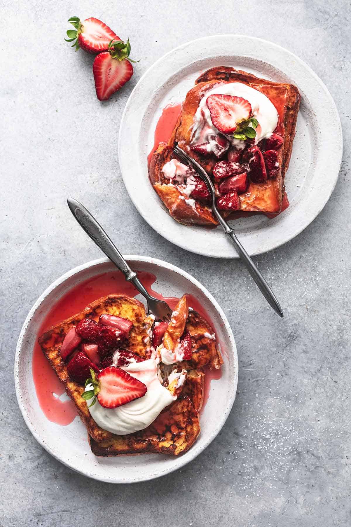 top view ofstrawberries and cream French toast on two plates topped with strawberry sauce, strawberries and whipped cream.