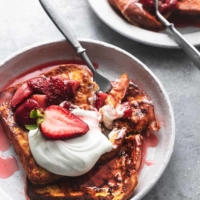 fork digging into stack of strawberry french toast with whipped cream on plate