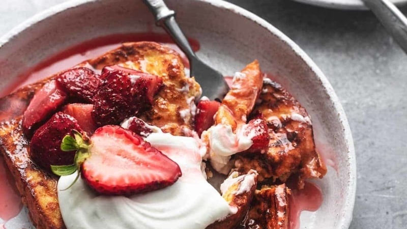 fork digging into stack of strawberry french toast with whipped cream on plate