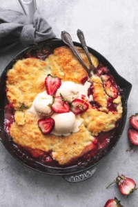 overhead strawberry cobbler in cast iron skillet topped with ice cream and fresh strawberries