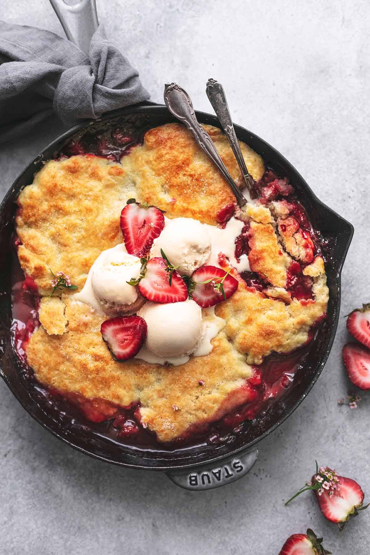 top view of strawberry cobbler in a cast iron skillet topped with ice cream and fresh strawberries.