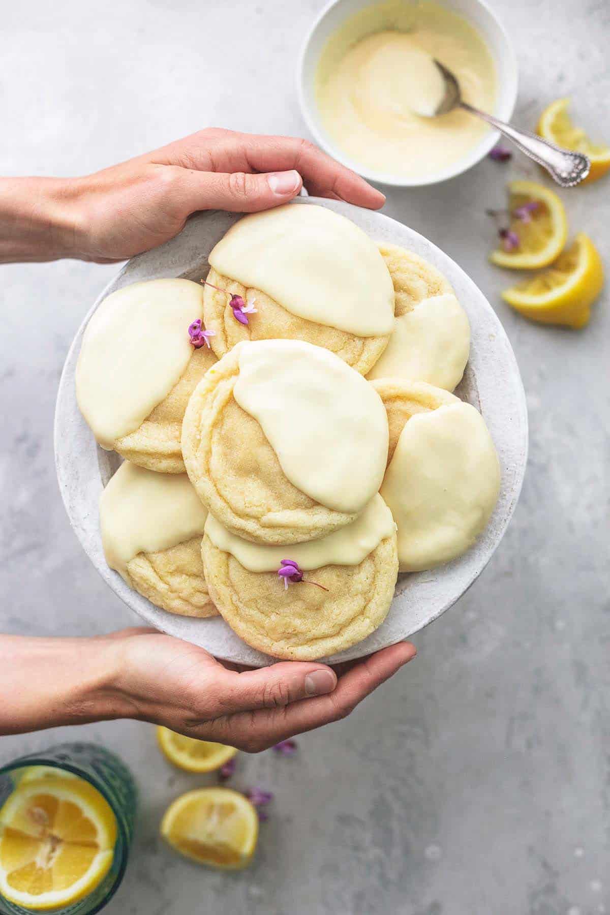 top view of hands holding plate of snow capped lemon cookies.