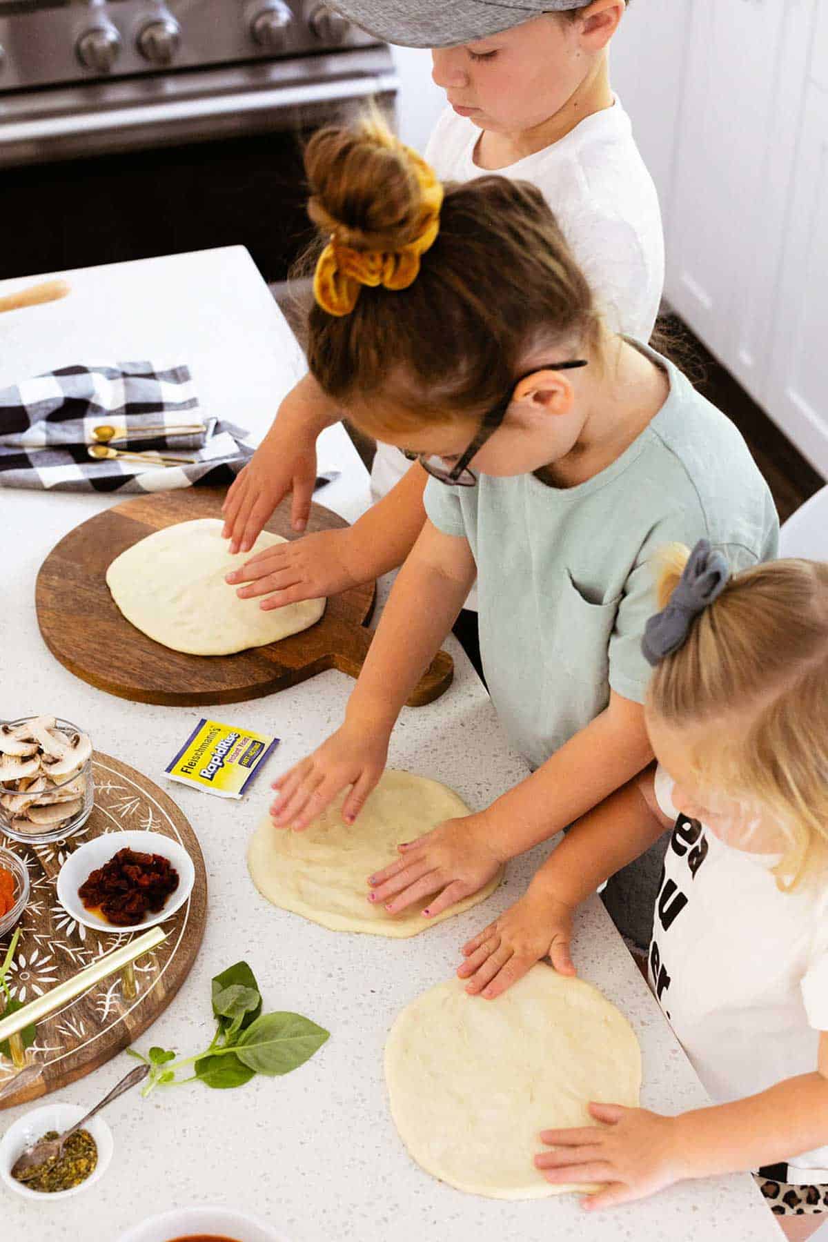 kids patting pizza dough for personal pizzas on countertop.